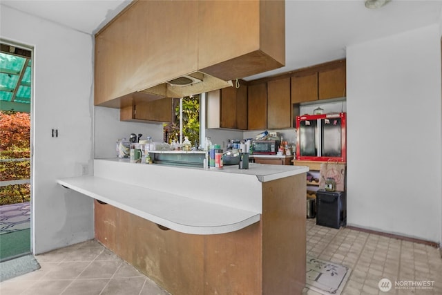 1412 N 40th St, Renton, WA 98056 - kitchen with stainless steel microwave, light countertops, a peninsula, brown cabinets, and light tile patterned floors