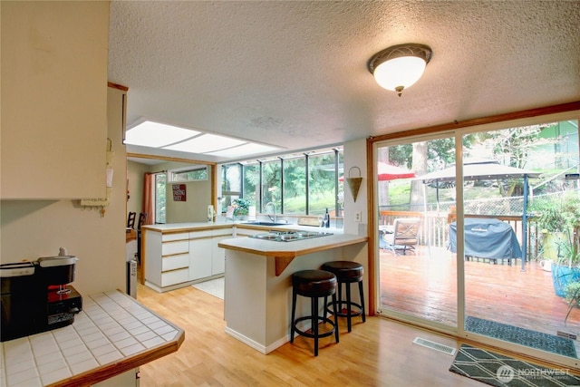 908 185th St SW, Lynnwood, WA 98037 - kitchen with a textured ceiling, a peninsula, light wood-style floors, tile counters, and a breakfast bar area