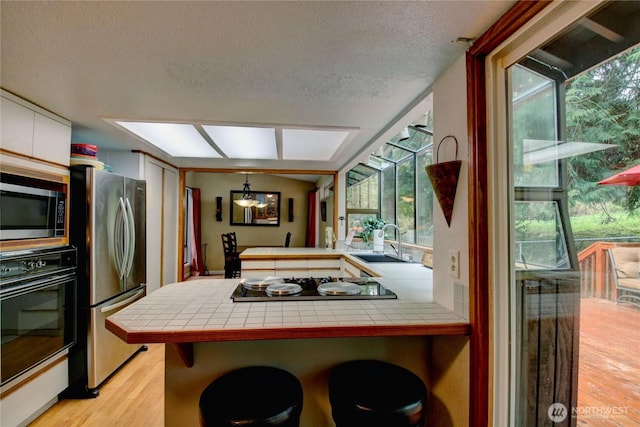 908 185th St SW, Lynnwood, WA 98037 - kitchen with black appliances, tile countertops, light wood-type flooring, a peninsula, and a textured ceiling