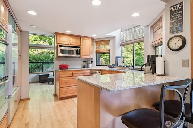 24230 218th Ave SE, Maple Valley, WA 98038 - kitchen featuring stainless steel microwave, a peninsula, light wood-type flooring, light stone counters, and a breakfast bar