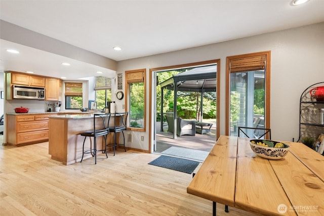 24230 218th Ave SE, Maple Valley, WA 98038 - kitchen with stainless steel microwave, light wood-style floors, recessed lighting, a breakfast bar, and light brown cabinetry