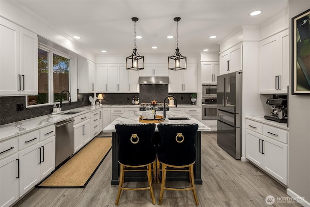 8907 NE 152nd Pl, Bothell, WA 98011 - kitchen featuring appliances with stainless steel finishes, under cabinet range hood, light wood finished floors, a kitchen island with sink, and recessed lighting