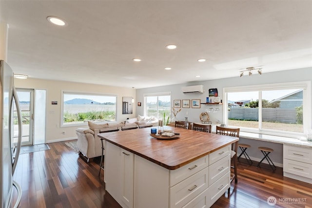 4452 Saltspring Dr, Ferndale, WA 98248 - kitchen featuring wooden counters, an AC wall unit, open floor plan, a breakfast bar, and white cabinetry