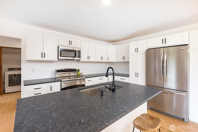 150 Sunland Dr, Sequim, WA 98382 - kitchen featuring stainless steel appliances, washer / dryer, light wood-style floors, white cabinetry, and a breakfast bar