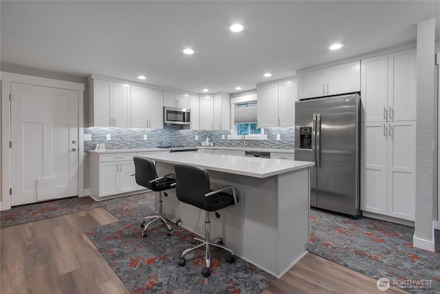 11108 Pilchuck Ct SE, Olympia, WA 98501 - kitchen featuring stainless steel appliances, wood finished floors, white cabinets, a kitchen breakfast bar, and a center island