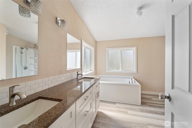 1303 Craig St W, Moses Lake, WA 98837 - bathroom with vaulted ceiling, wood finished floors, decorative backsplash, double vanity, and a textured ceiling