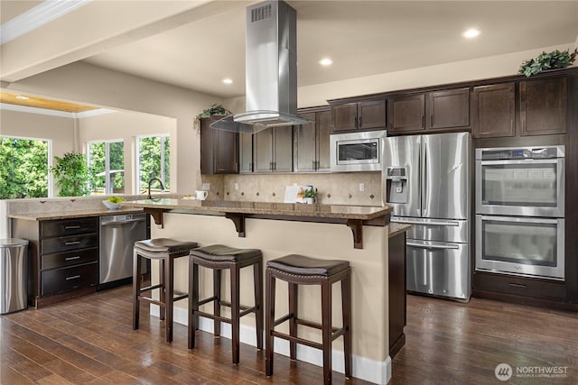21230 SE 258th Pl, Maple Valley, WA 98038 - kitchen featuring appliances with stainless steel finishes, island exhaust hood, dark brown cabinets, a kitchen bar, and light stone countertops