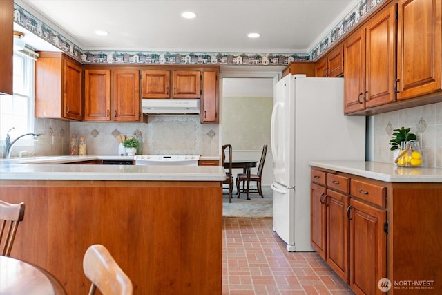 1175 SW Lopez Dr, Oak Harbor, WA 98277 - kitchen with under cabinet range hood, brick patterned flooring, brown cabinets, light countertops, and crown molding