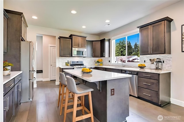 16311 5th Dr SE, Bothell, WA 98012 - kitchen with appliances with stainless steel finishes, dark brown cabinetry, a breakfast bar area, tasteful backsplash, and recessed lighting