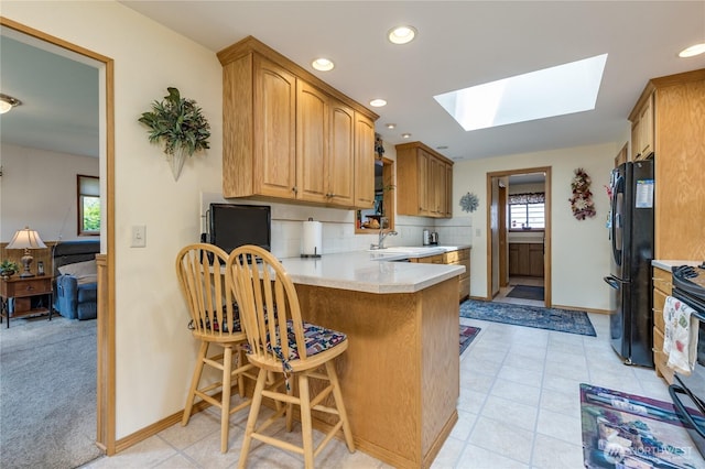 1023 E Maple St, Kent, WA 98030 - kitchen with freestanding refrigerator, a skylight, light countertops, a peninsula, and tasteful backsplash