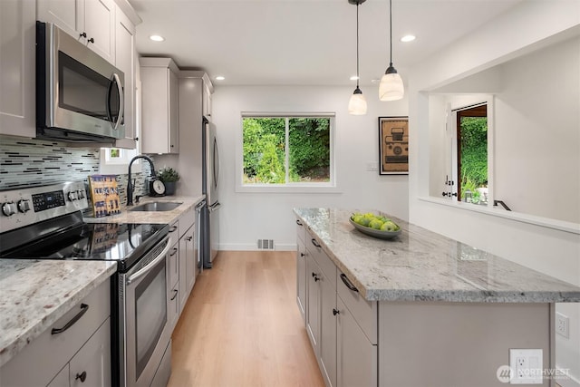 4886 24th Ave S, Seattle, WA 98108 - kitchen with stainless steel appliances, a center island, light wood finished floors, recessed lighting, and light stone counters