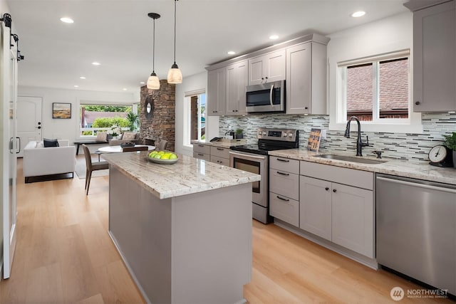 4886 24th Ave S, Seattle, WA 98108 - kitchen featuring appliances with stainless steel finishes, gray cabinets, light wood-type flooring, a center island, and decorative backsplash