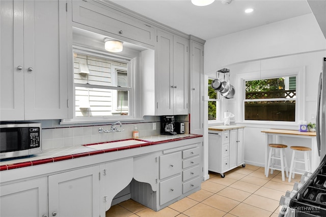 1916 11th Ave W, Seattle, WA 98119 - kitchen featuring stainless steel microwave, backsplash, light tile patterned floors, and tile counters