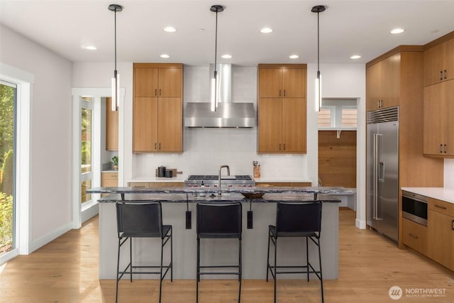 21025 SE 80th St, Issaquah, WA 98027 - kitchen with wall chimney range hood, built in appliances, light wood-type flooring, backsplash, and dark stone countertops