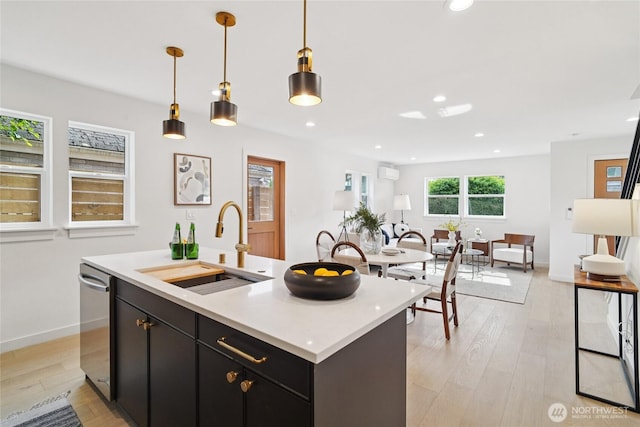 8227 Latona Ave NE, Seattle, WA 98115 - kitchen featuring dark cabinets, light countertops, light wood-type flooring, a center island with sink, and decorative light fixtures
