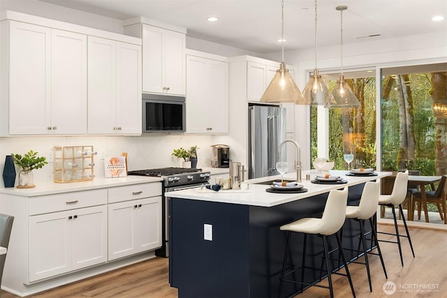 13446 HS4 NE 112th Pl, Redmond, WA 98052 - kitchen with appliances with stainless steel finishes, an island with sink, a breakfast bar, light countertops, and light wood-type flooring