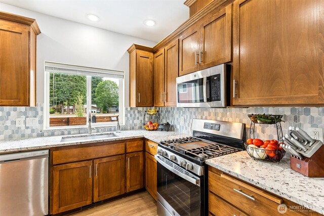 815 6th Ave SW, Olympia, WA 98512 - kitchen with stainless steel appliances, light stone countertops, brown cabinets, tasteful backsplash, and light wood-style flooring