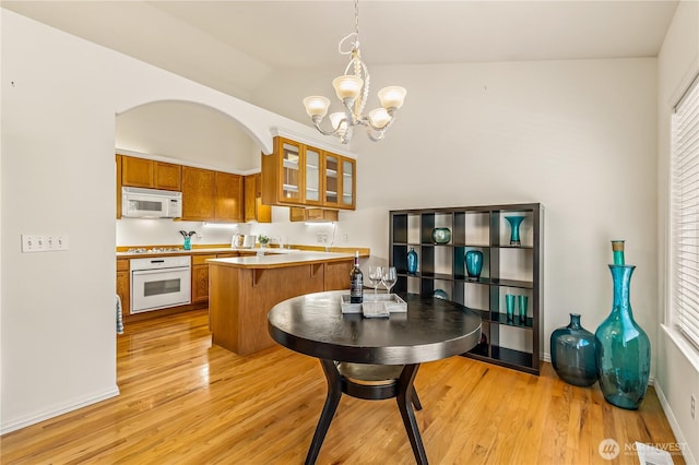 8221 53rd Ave W Unit 15C, Mukilteo, WA 98275 - kitchen featuring white appliances, brown cabinetry, a chandelier, a peninsula, and glass insert cabinets
