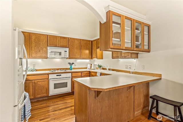 8221 53rd Ave W Unit 15C, Mukilteo, WA 98275 - kitchen featuring white appliances, a peninsula, brown cabinets, light wood-type flooring, and glass insert cabinets