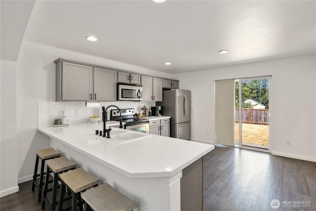 20008 99th Ave E, Graham, WA 98338 - kitchen featuring appliances with stainless steel finishes, light countertops, gray cabinetry, dark wood-type flooring, and a breakfast bar