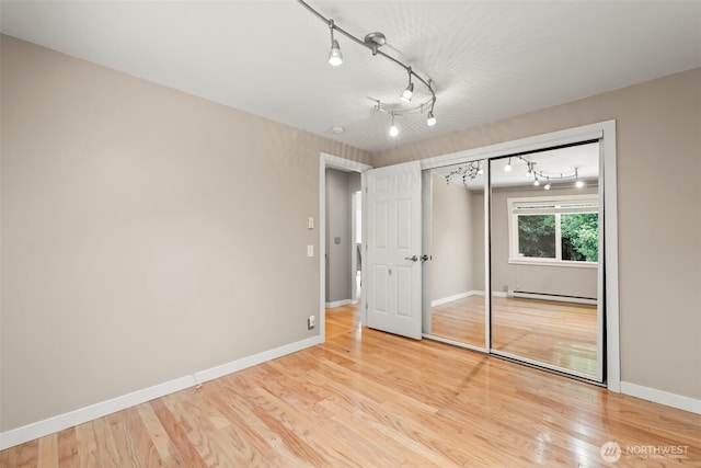 12170 Viewcrest Pl NE, Bainbridge Island, WA 98110 - unfurnished bedroom with baseboard heating, track lighting, a closet, and light wood-style floors