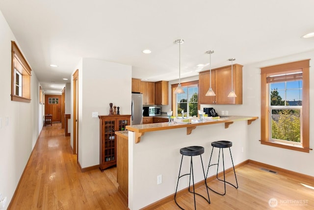4415 40th Ave SW, Seattle, WA 98116 - kitchen featuring appliances with stainless steel finishes, a peninsula, a breakfast bar area, light wood finished floors, and light countertops