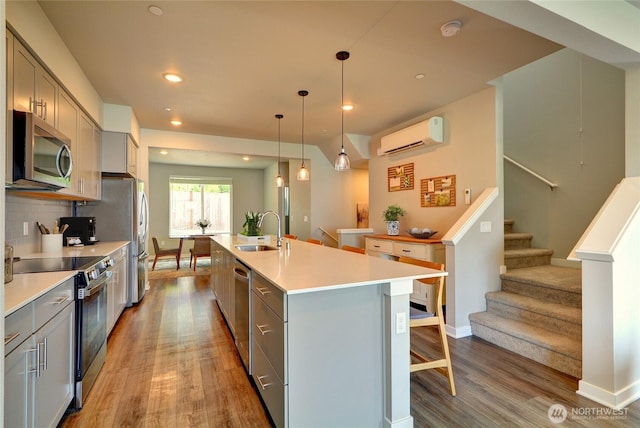 2014 101st Ave SE Unit 6, Lake Stevens, WA 98258 - kitchen featuring appliances with stainless steel finishes, gray cabinets, a wall unit AC, light wood-style flooring, and a center island with sink