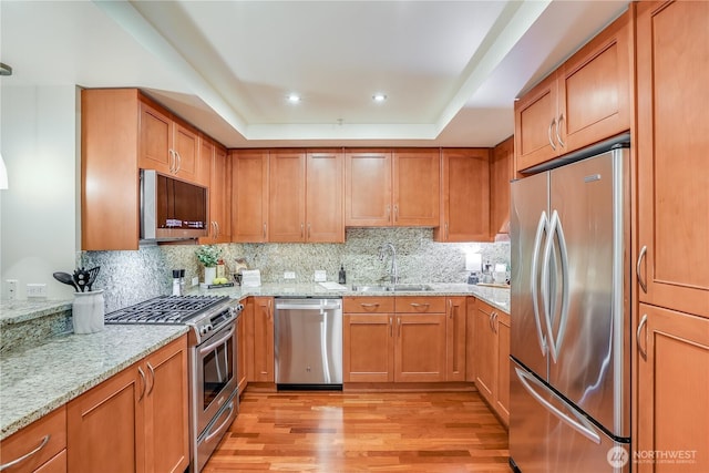 10650 NE 9th Pl Unit 3208, Bellevue, WA 98004 - kitchen featuring appliances with stainless steel finishes, light wood-type flooring, light stone counters, brown cabinetry, and a tray ceiling