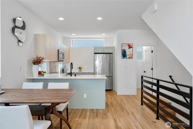 2620 NW 62nd St Unit B, Seattle, WA 98107 - kitchen featuring appliances with stainless steel finishes, light wood-style flooring, light countertops, a peninsula, and recessed lighting