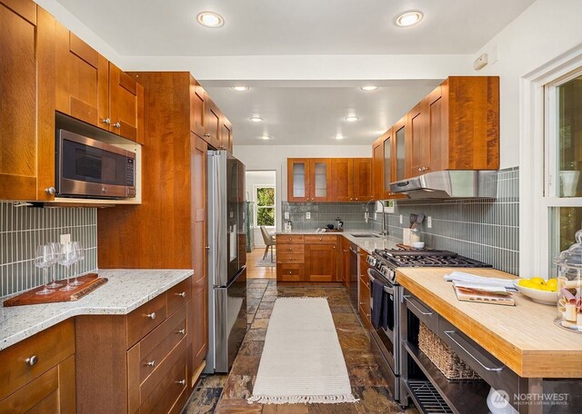3112 NE 65th St, Seattle, WA 98115 - kitchen featuring appliances with stainless steel finishes, backsplash, under cabinet range hood, stone tile floors, and recessed lighting