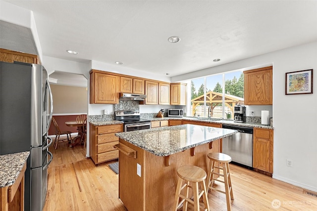 9321 339th St S Unit 5, Roy, WA 98580 - kitchen featuring stainless steel appliances, under cabinet range hood, a center island, light stone counters, and light wood-type flooring