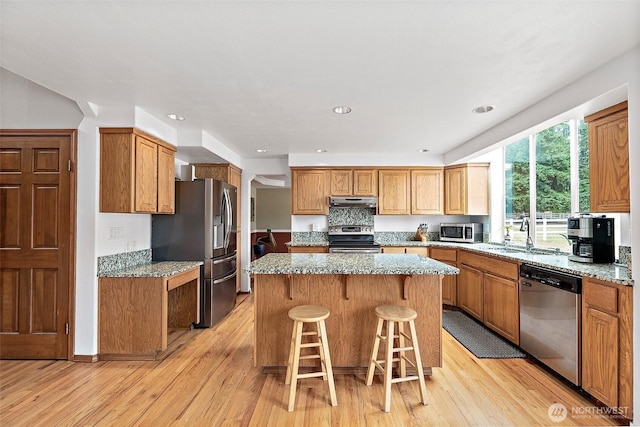 9321 339th St S Unit 5, Roy, WA 98580 - kitchen with appliances with stainless steel finishes, a kitchen island, light wood finished floors, a kitchen bar, and light stone counters
