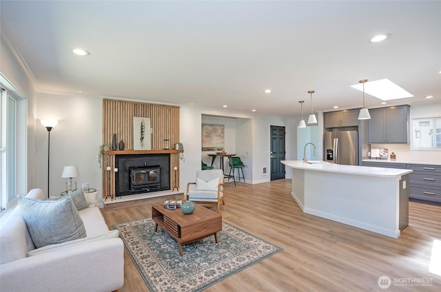 15512 Elm St E, Sumner, WA 98390 - living room featuring recessed lighting, light wood-type flooring, ornamental molding, a skylight, and a glass covered fireplace