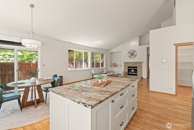 18130 Sunrise Ridge Ave NE, Poulsbo, WA 98370 - kitchen featuring light wood-style floors, white cabinets, a center island, vaulted ceiling, and a stone fireplace