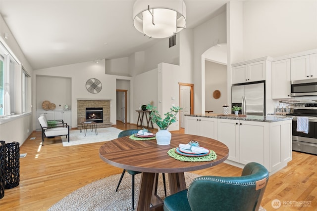 18130 Sunrise Ridge Ave NE, Poulsbo, WA 98370 - dining space with a warm lit fireplace, light wood finished floors, and high vaulted ceiling
