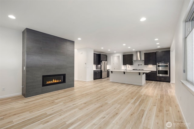 12619 176th St E, Puyallup, WA 98374 - kitchen with wall chimney range hood, appliances with stainless steel finishes, a breakfast bar, open floor plan, and light wood finished floors