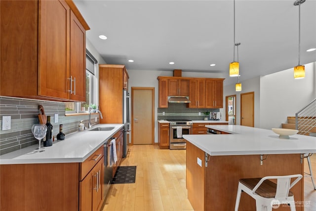 3800 SW Holden St, Seattle, WA 98126 - kitchen featuring stainless steel appliances, under cabinet range hood, decorative backsplash, brown cabinetry, and recessed lighting