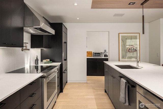 2241 Fairview Ave E Unit B, Seattle, WA 98102 - kitchen featuring stainless steel appliances, wall chimney range hood, light wood-style flooring, dark cabinets, and light countertops