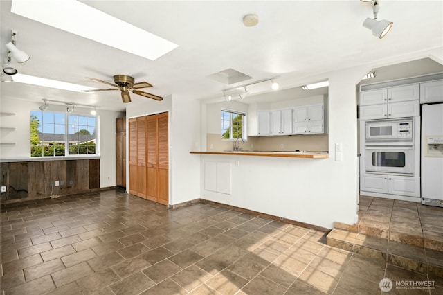 1037 Harding St, Enumclaw, WA 98022 - kitchen with white appliances, a skylight, rail lighting, ceiling fan, and white cabinetry