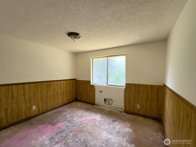 6420 NE Nelson St, Suquamish, WA 98392 - empty room featuring wainscoting, wood walls, a textured ceiling, and unfinished concrete flooring