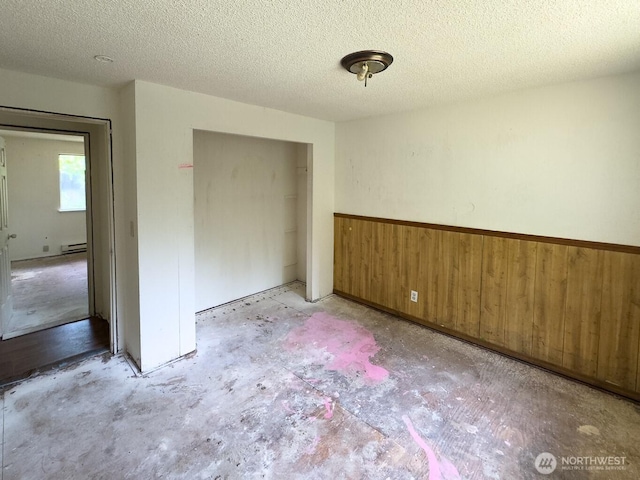 6420 NE Nelson St, Suquamish, WA 98392 - unfurnished bedroom featuring concrete flooring, a closet, wood walls, a baseboard radiator, and a textured ceiling
