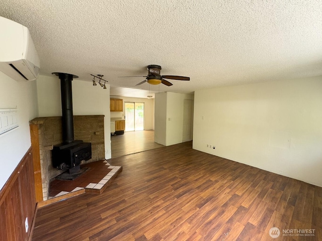 6420 NE Nelson St, Suquamish, WA 98392 - unfurnished living room featuring a wall unit AC, wood finished floors, ceiling fan, a wood stove, and a textured ceiling