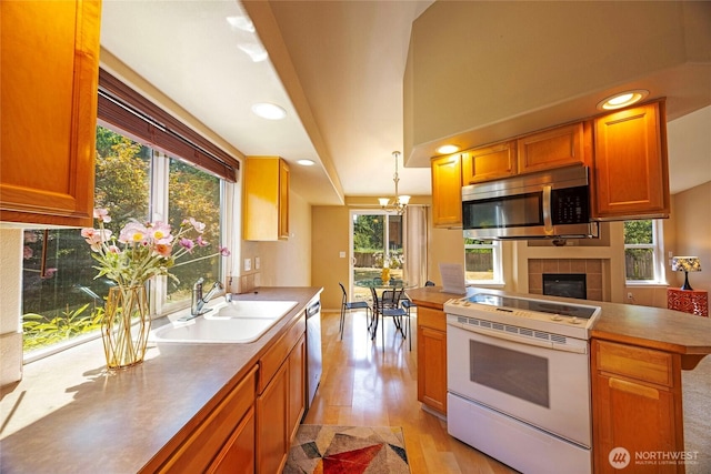 2218 143rd Street Ct S, Spanaway, WA 98387 - kitchen featuring appliances with stainless steel finishes, light wood-style floors, a tiled fireplace, a chandelier, and decorative light fixtures