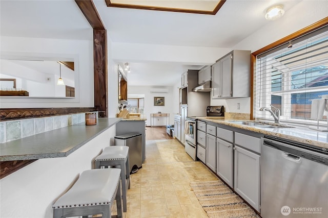 10208 D St E, Tacoma, WA 98445 - kitchen featuring appliances with stainless steel finishes, gray cabinets, an AC wall unit, a kitchen bar, and under cabinet range hood