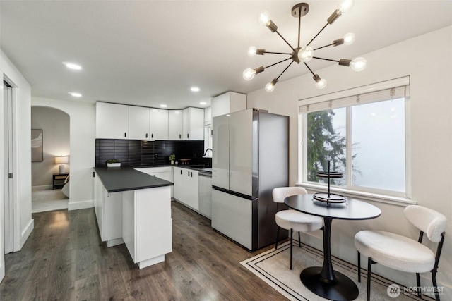 5467 16th Ave SW, Seattle, WA 98106 - kitchen featuring freestanding refrigerator, dark countertops, white cabinetry, arched walkways, and tasteful backsplash