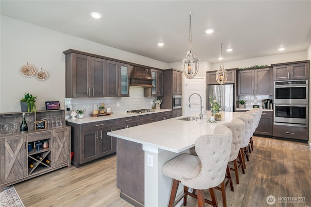 1448 101st Ave SE, Lake Stevens, WA 98258 - kitchen with appliances with stainless steel finishes, premium range hood, dark brown cabinetry, a kitchen bar, and backsplash