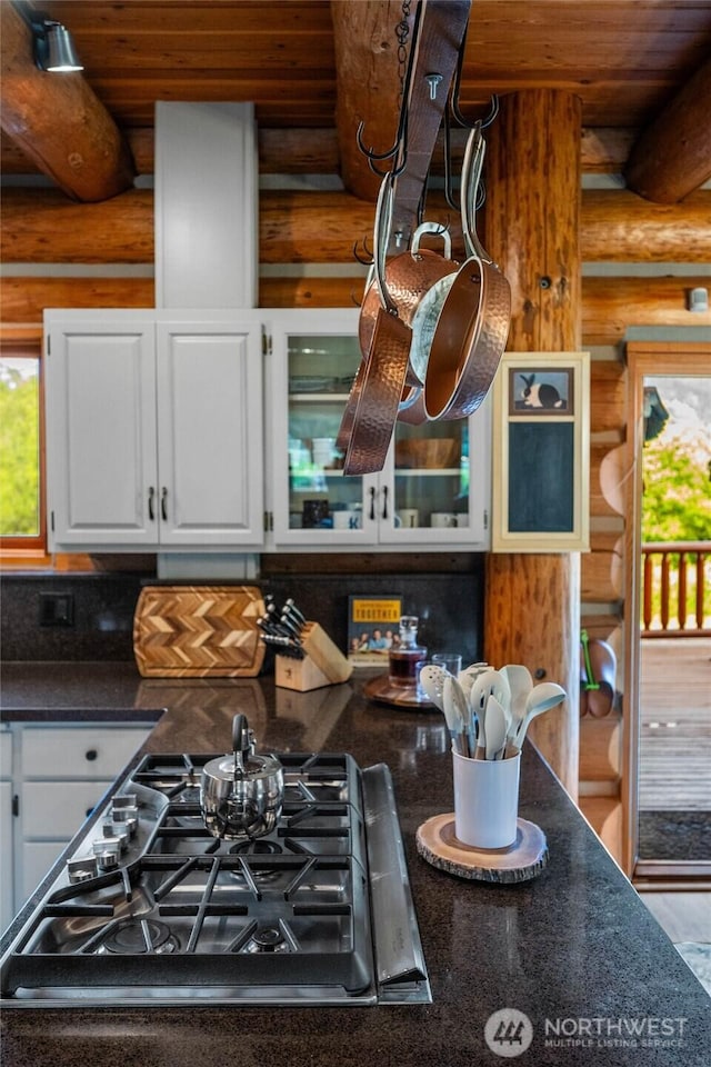 3130 S Bay Vista Dr, Sedro Woolley, WA 98284 - kitchen view of log walls, stainless steel gas stovetop, dark countertops, white cabinetry, and glass insert cabinets