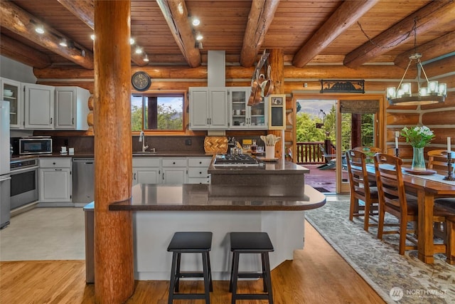 3130 S Bay Vista Dr, Sedro Woolley, WA 98284 - kitchen featuring stainless steel appliances, rustic walls, a wood ceiling with exposed beams, dark countertops, and glass insert cabinets