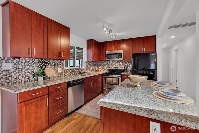 18256 45th Ave S, Seatac, WA 98188 - kitchen with stainless steel appliances, light wood-style floors, light stone countertops, a kitchen island, and reddish brown cabinets