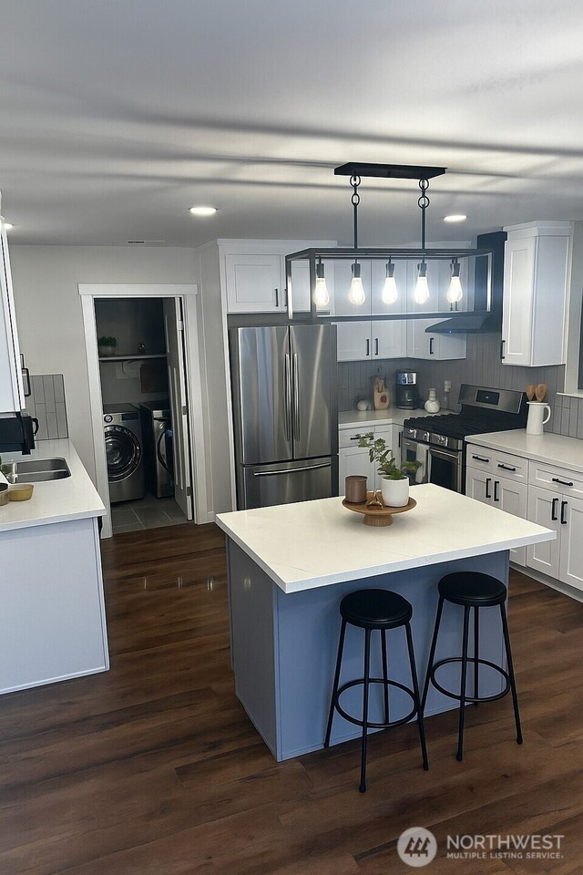 2011 85th Street Ct E, Tacoma, WA 98445 - kitchen featuring stainless steel appliances, washing machine and clothes dryer, a breakfast bar area, white cabinetry, and dark wood finished floors